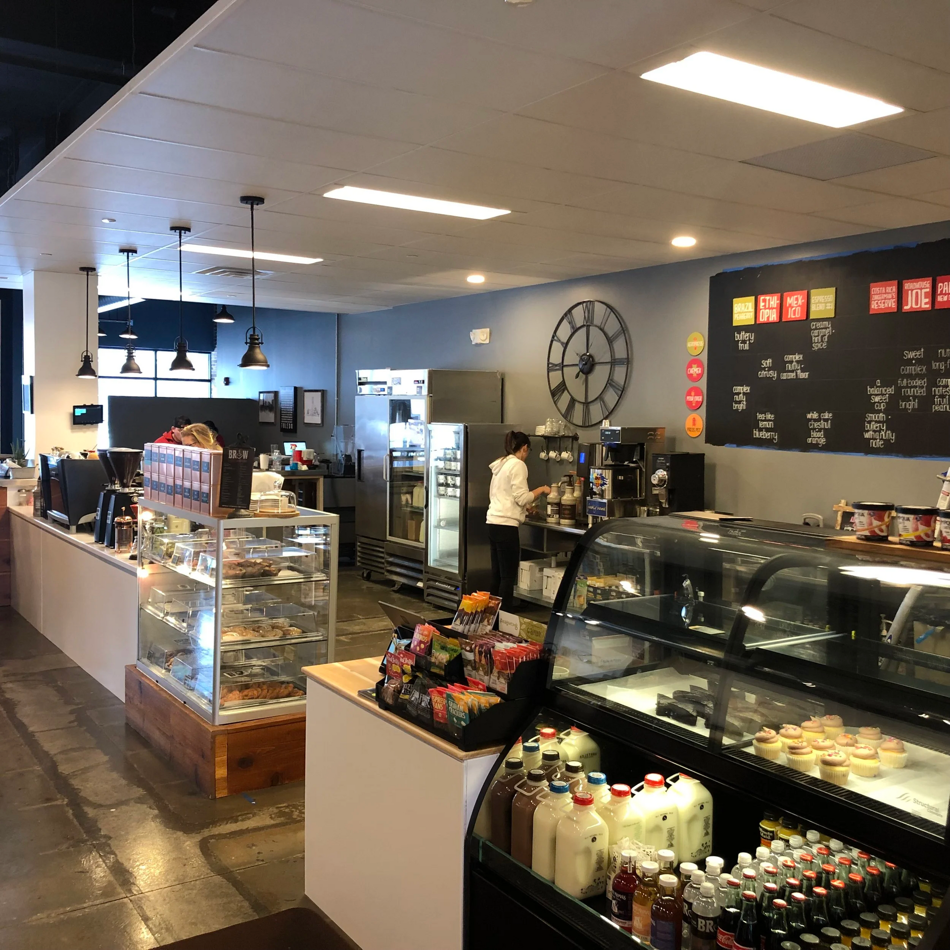 Interior of a coffee shop with a customer, display cases of pastries, and a menu board.