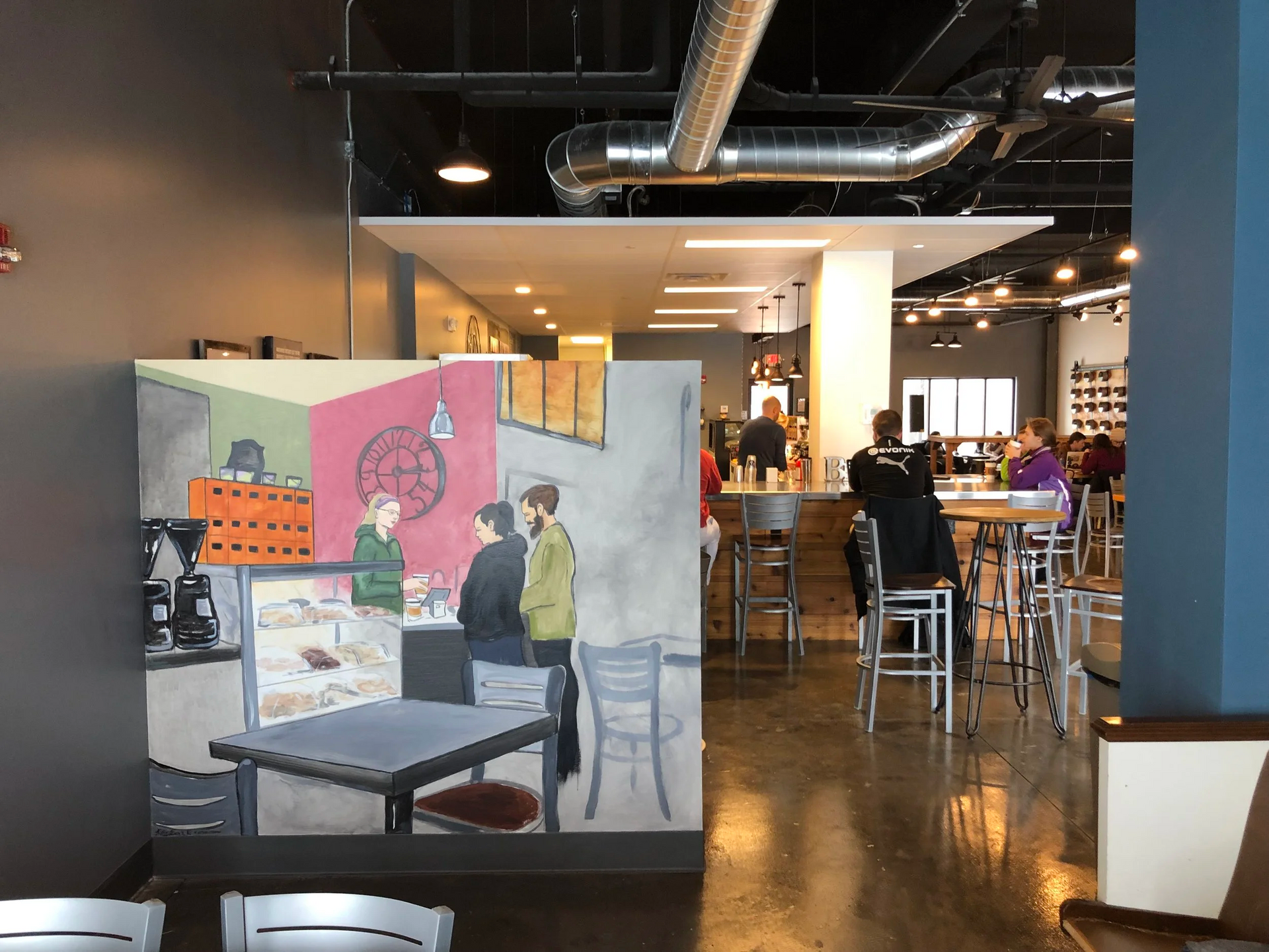 A cafe interior with artwork of a cafe scene, people at tables, bar, and reflective flooring.