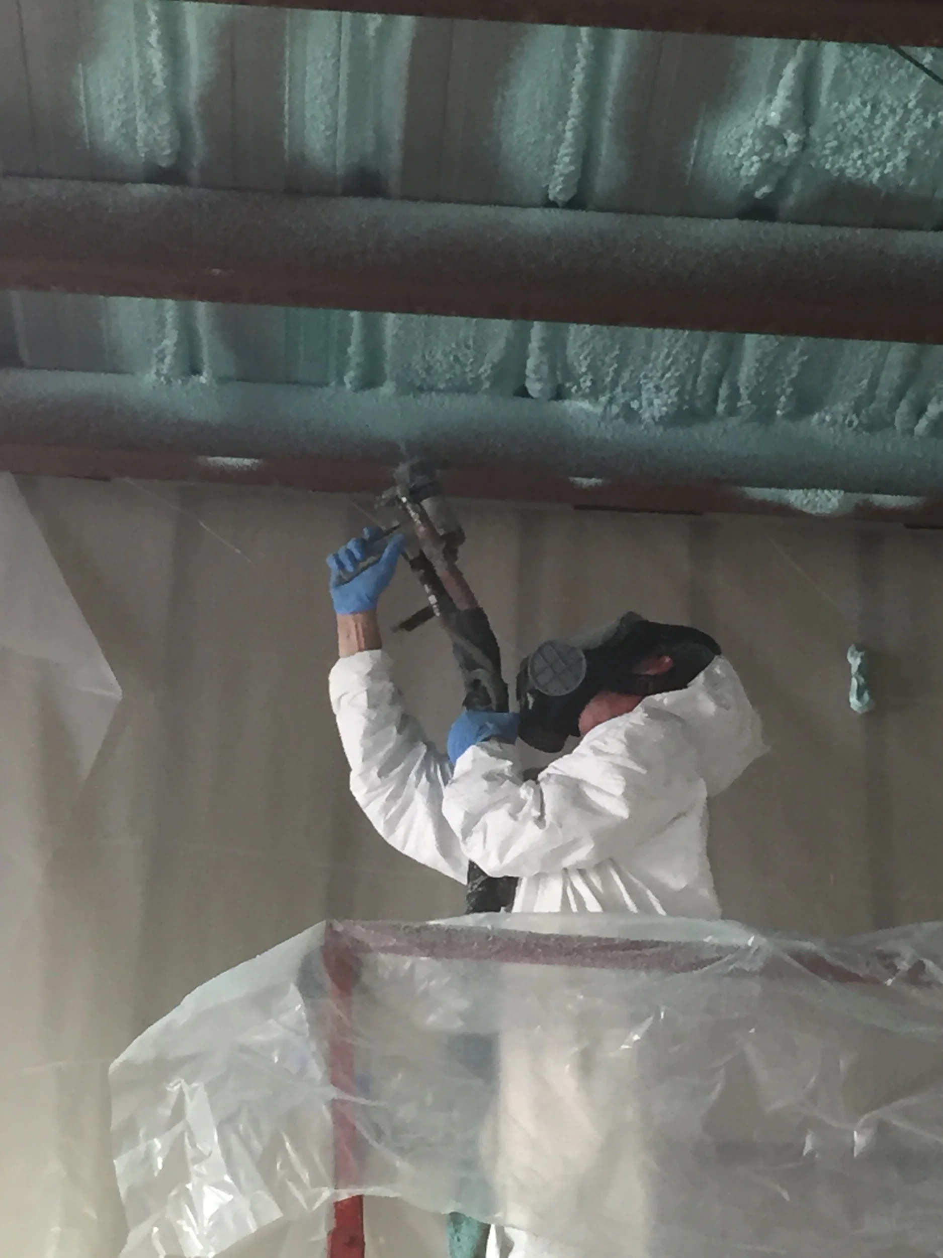 Person in protective suit spraying insulation on a ceiling.