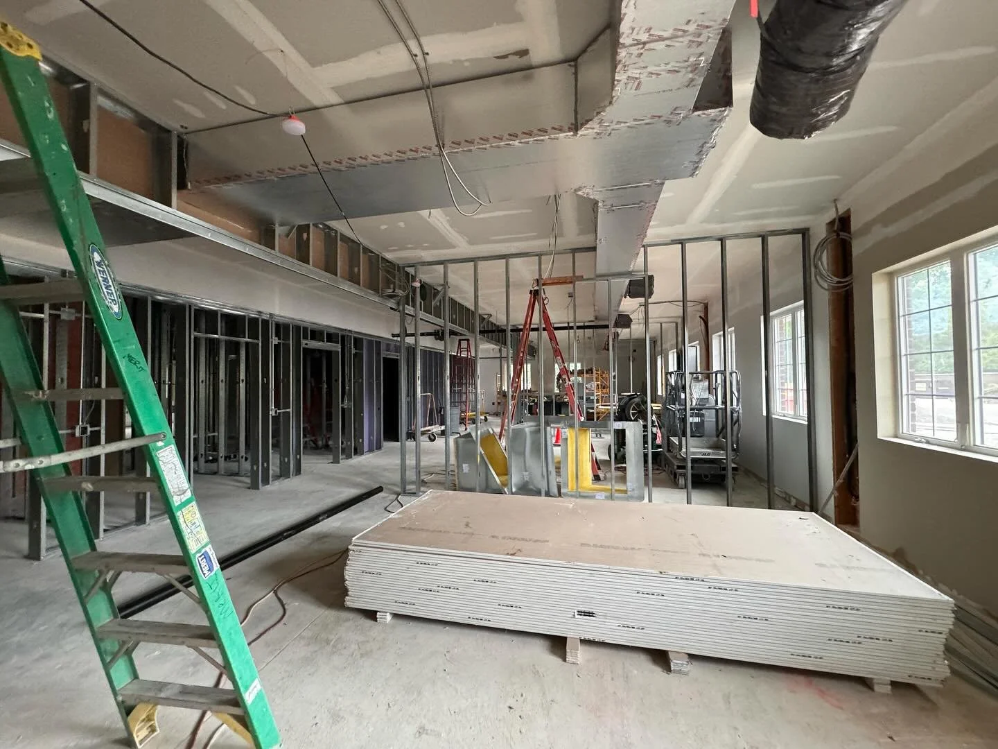 Interior construction site with metal framing, drywall, and a green ladder.