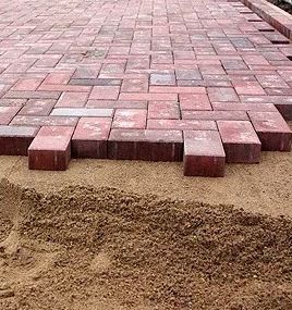 Red brick pavers being laid on a bed of sand for a walkway or patio.