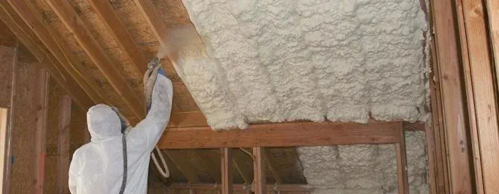 Person in protective suit spraying insulation into an attic.