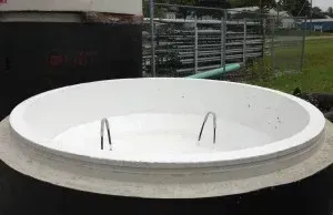 Open white circular tank with metal handles, in an outdoor setting.