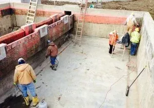 Construction workers inside a concrete structure, using tools. Some are spraying, others observing. Red and orange accents.