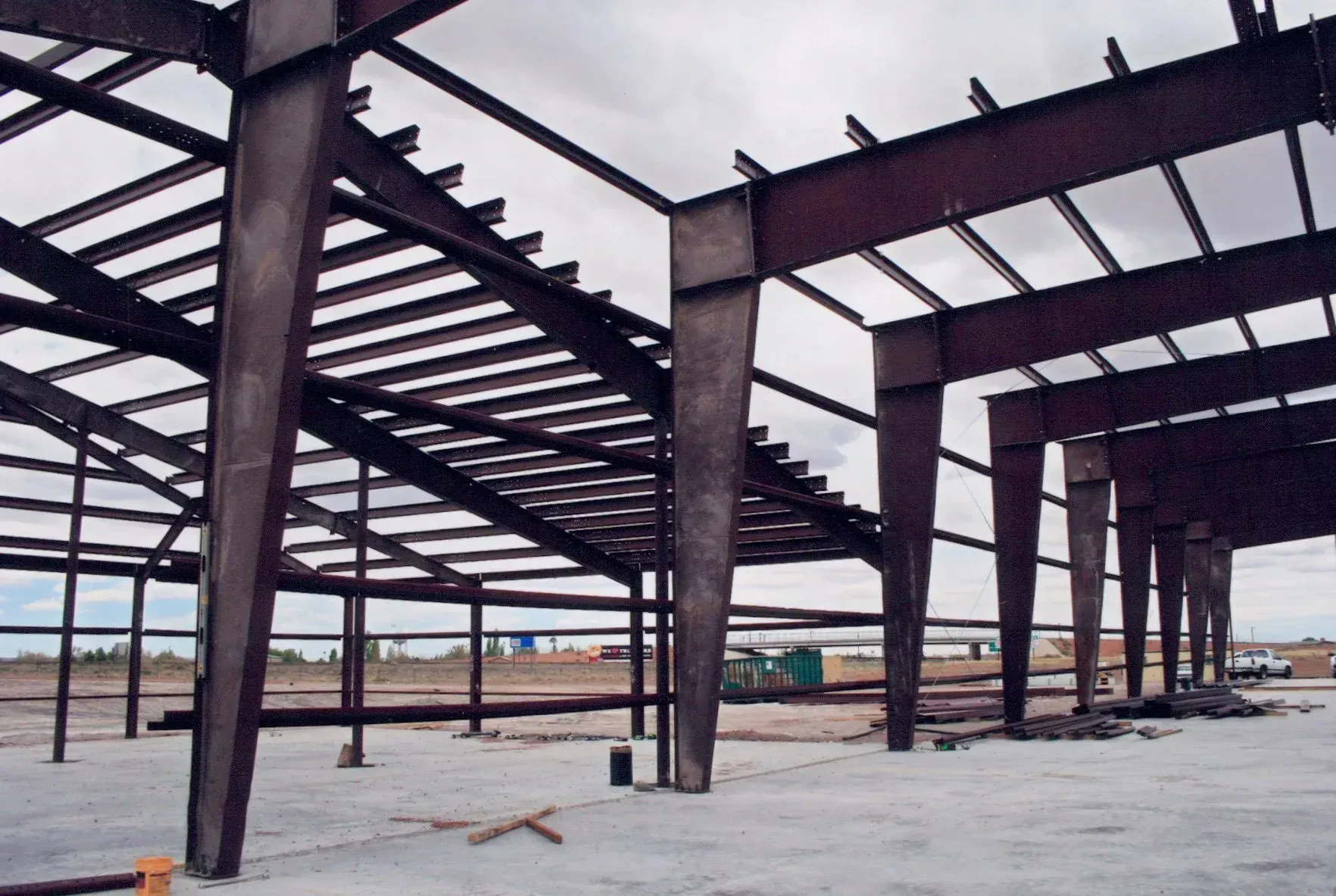 Steel framework of a building under construction, showing beams and columns against a cloudy sky.