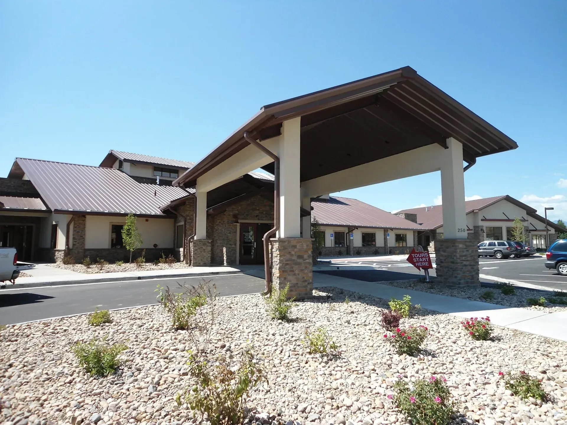 Exterior view of a single-story building with a covered entrance, tan exterior, and a brown metal roof.