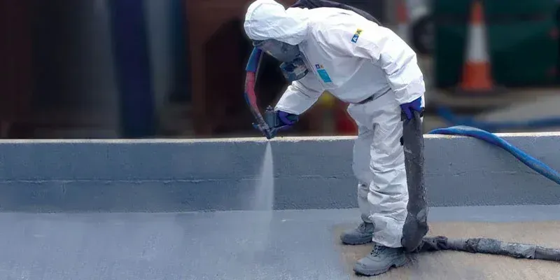 Person in protective suit spraying a surface with a hose.