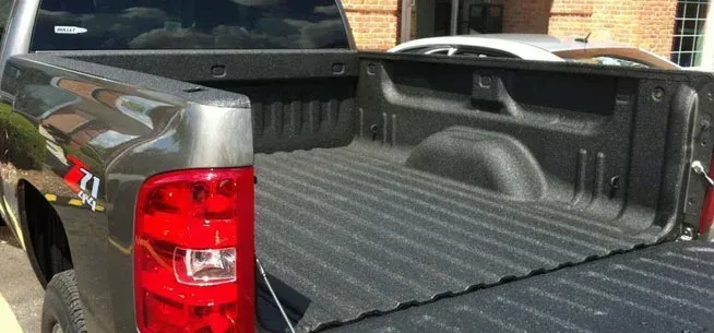 A close-up view of an empty, dark-grey pickup truck bed, showing the ribbed surface and side walls.