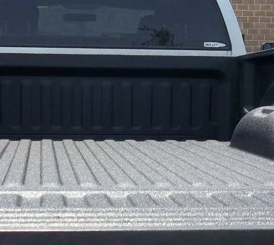 Truck bed interior with textured liner; back window and cab visible, black and gray tones.