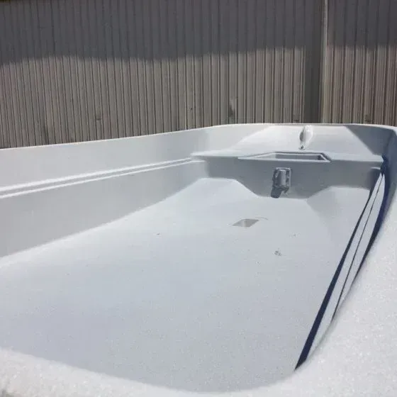 White boat interior with bench and metal fixture, against a gray fence.