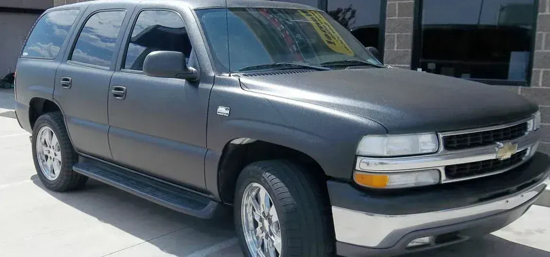 Dark gray SUV parked on a sunny day. Chrome wheels and trim, matte finish.
