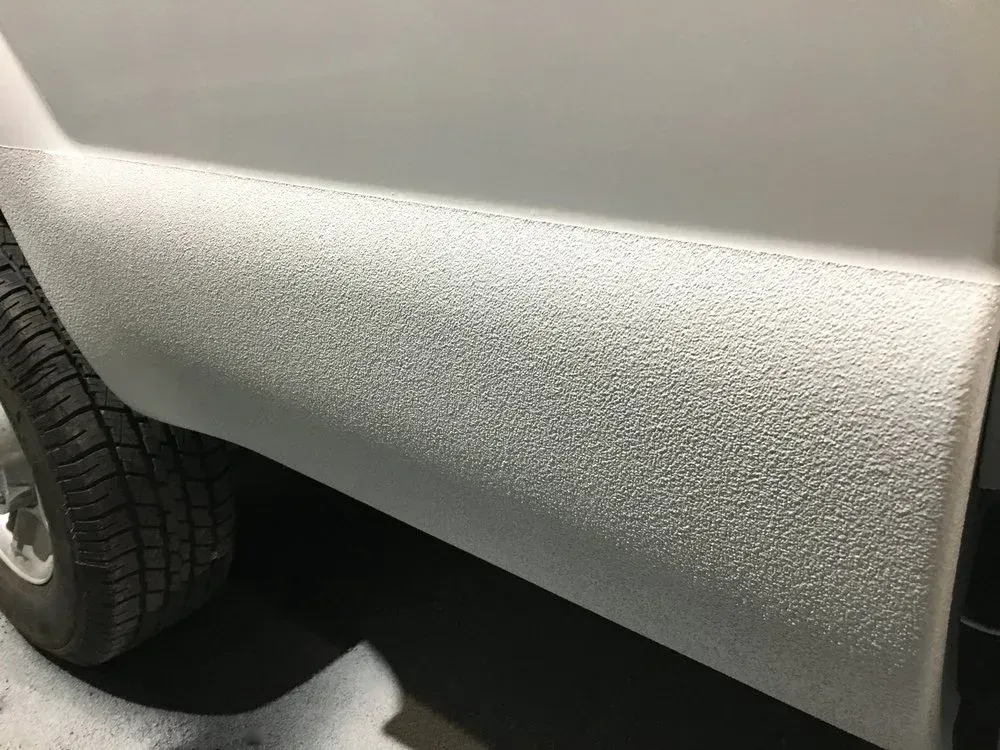 Textured white coating on the lower side of a vehicle, near a tire.