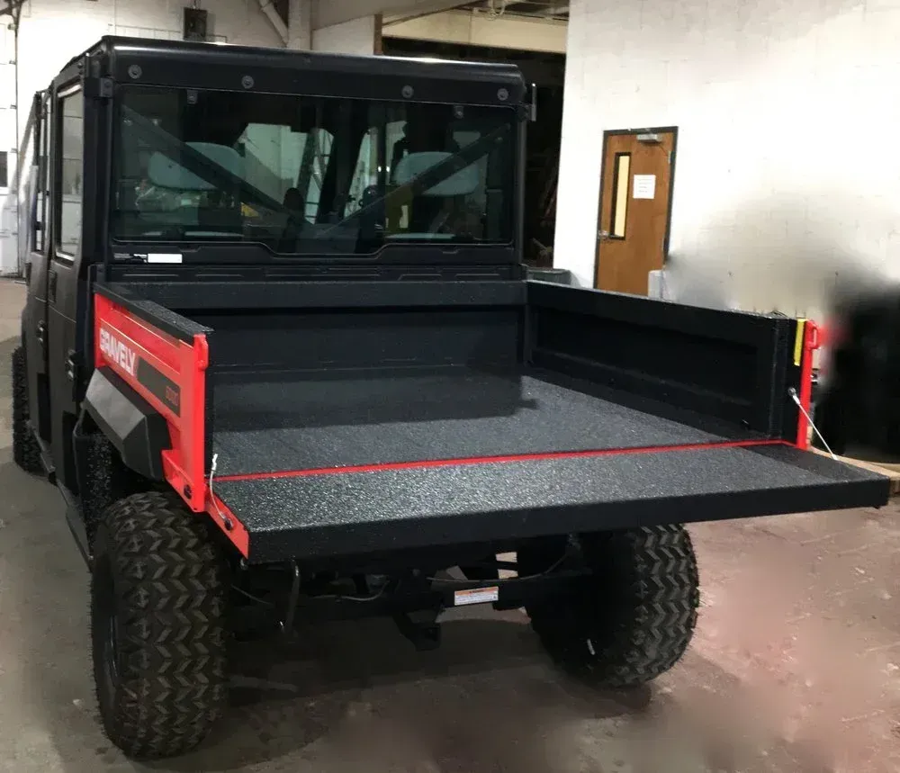 Black utility vehicle with open red-trimmed bed, parked indoors.