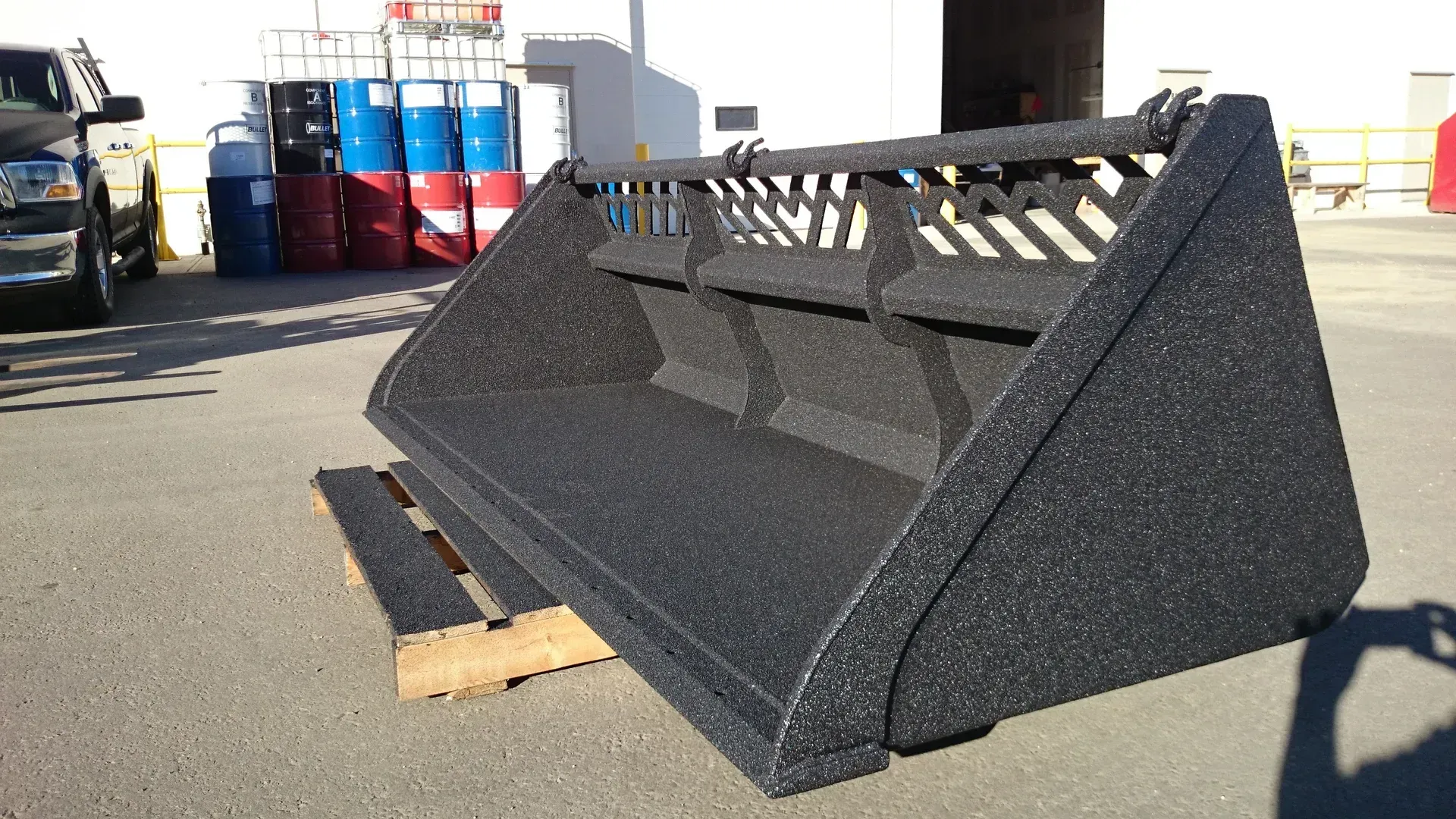 Black skid steer bucket on a wooden pallet, outdoors.