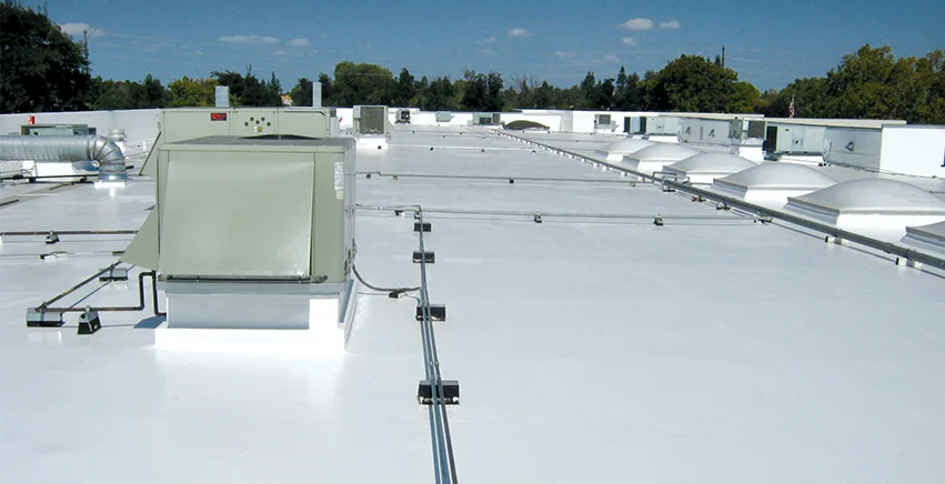 White commercial roof with equipment and skylights. Blue sky.