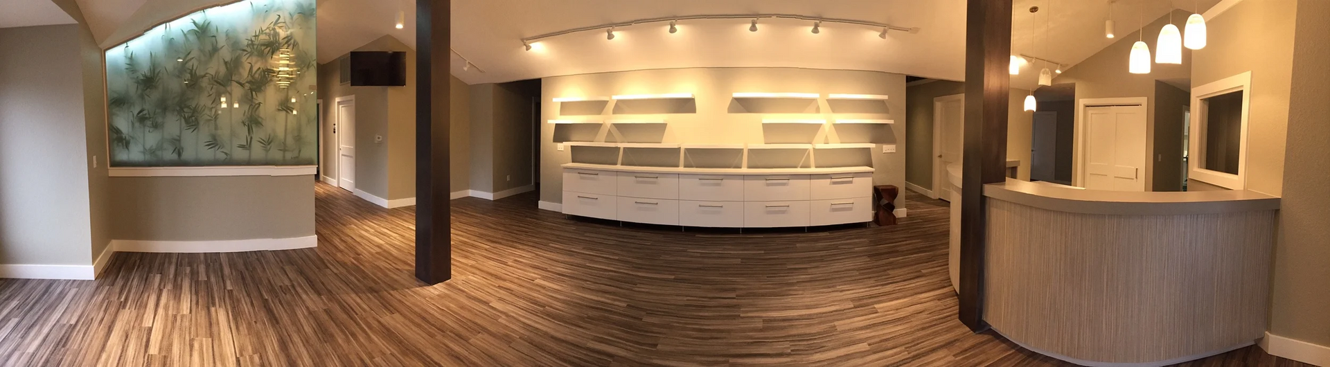 A room with white display shelves, a curved reception desk, and brown flooring.