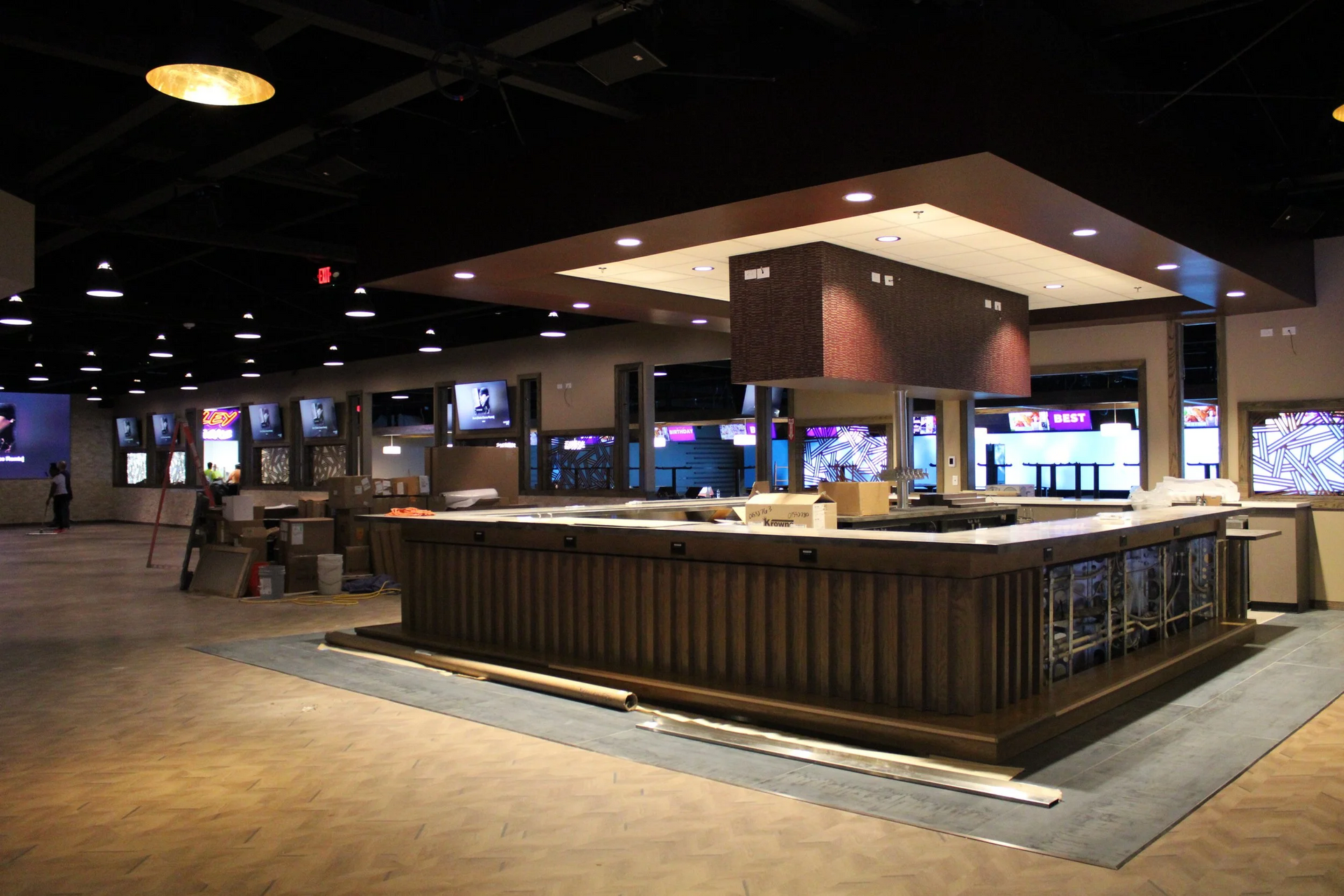 Bar under construction with multiple TVs, brown wood bar, and neutral walls.
