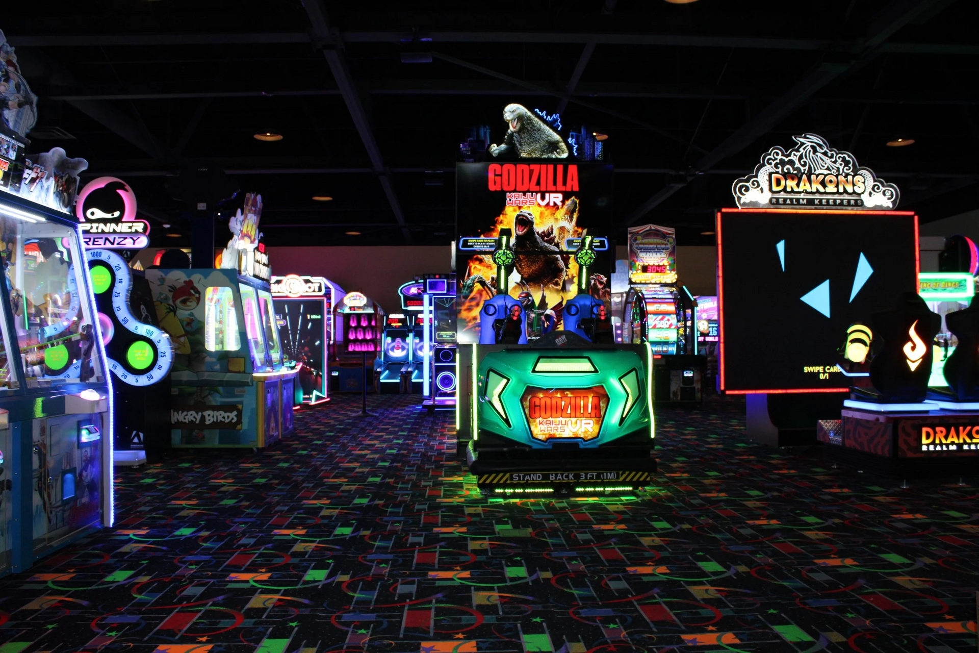 Arcade interior, brightly lit games, Godzilla arcade game, colorful lights, patterned carpet.