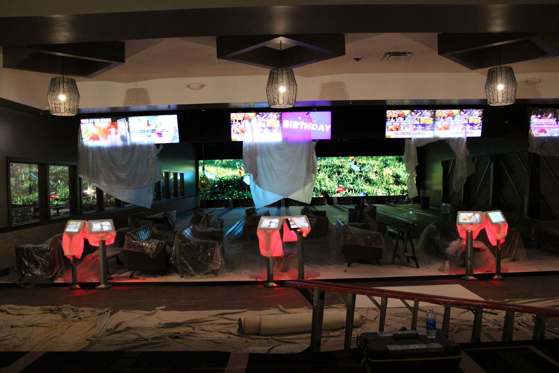 Interior of a restaurant under construction with TVs, kiosks, and protective coverings.