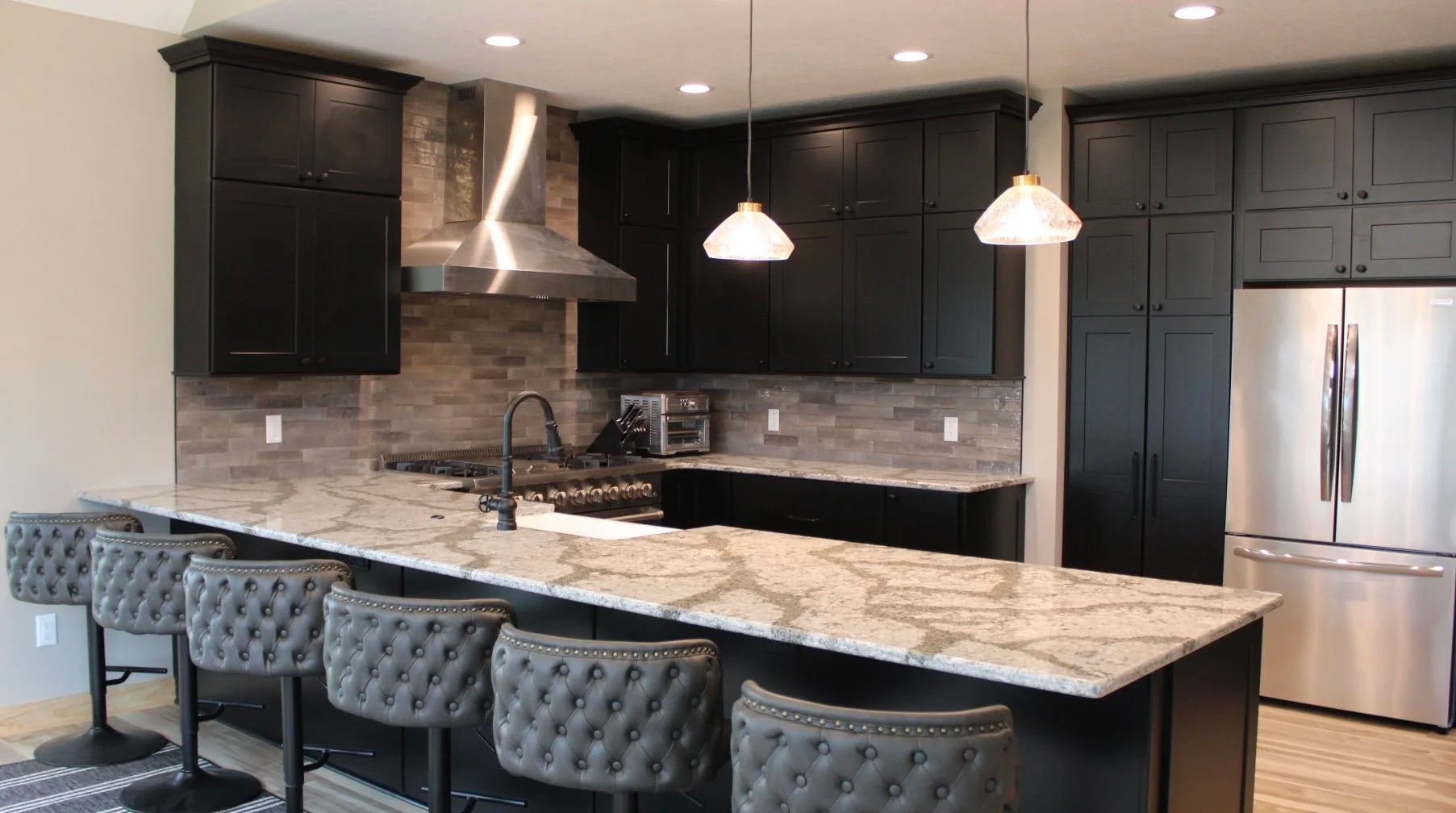 Dark kitchen with granite countertops, black cabinets, stainless steel appliances, and bar stools.