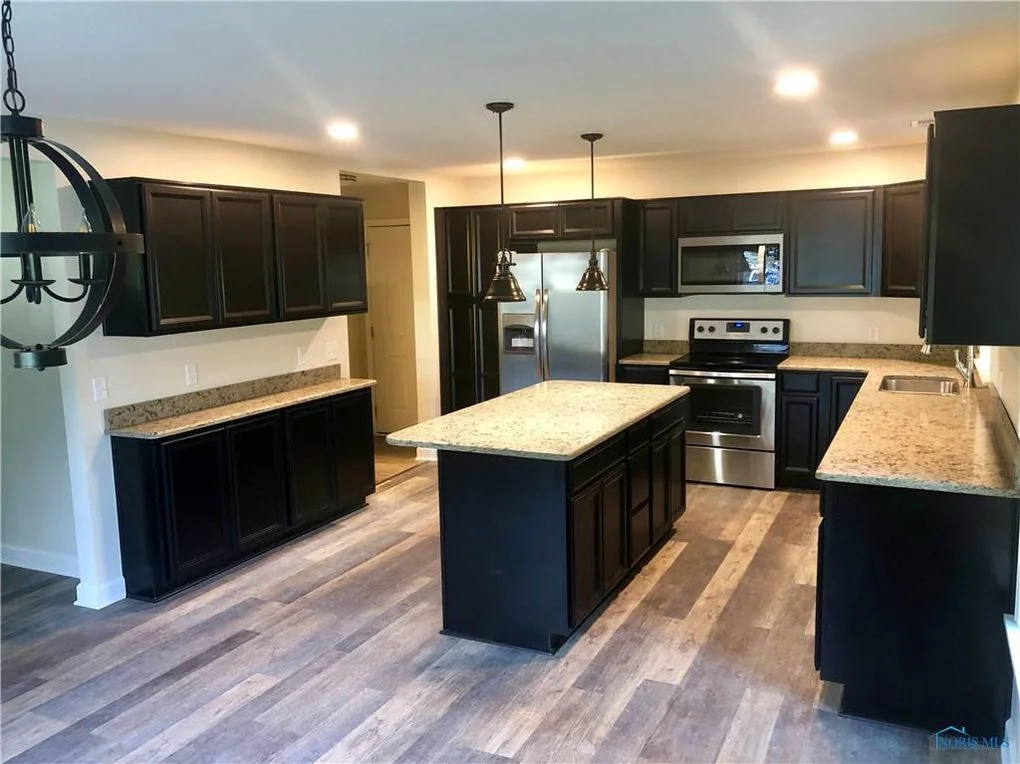 Black kitchen with island, stainless steel appliances, and light granite countertops.