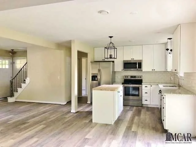 Modern kitchen with white cabinets, stainless steel appliances, and wood-look flooring.