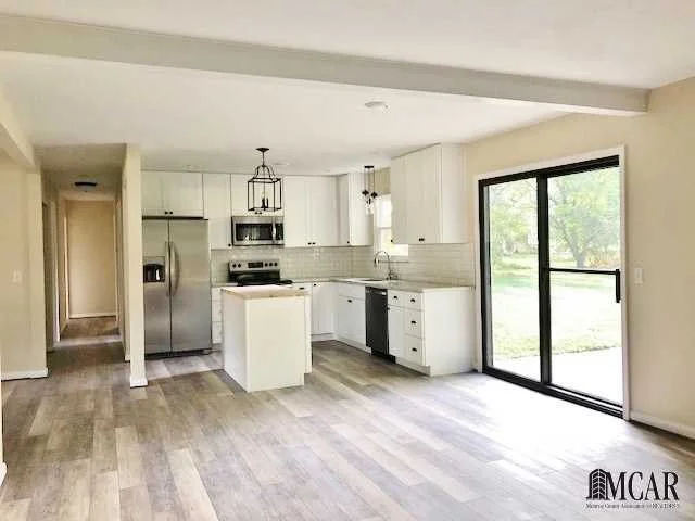 Open-concept kitchen with white cabinets, stainless steel appliances, and sliding glass door.
