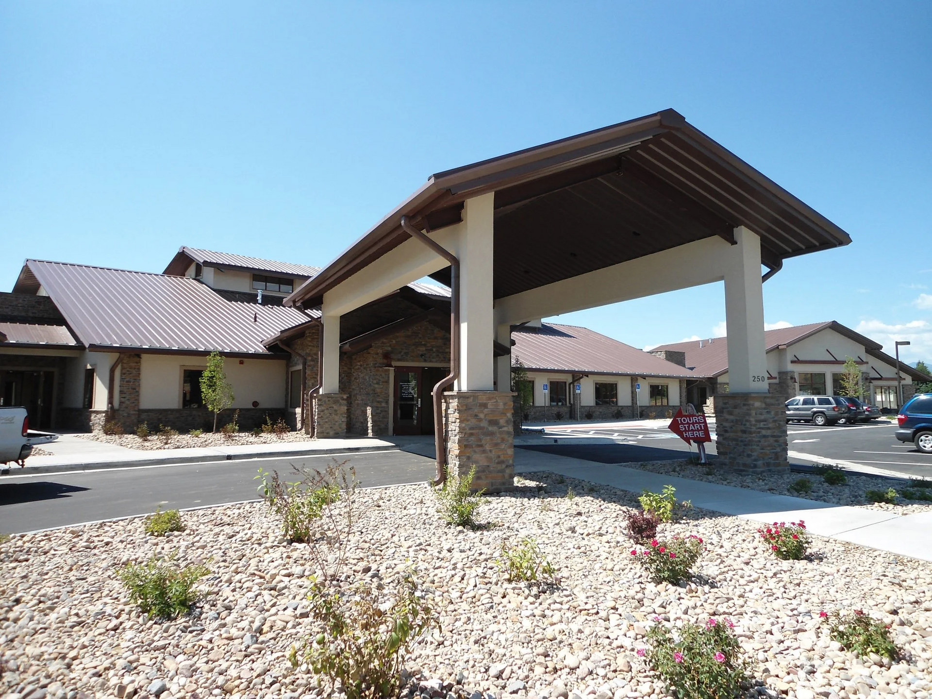 Entrance to a low, modern building with a covered walkway. Beige and stone exterior, blue sky.