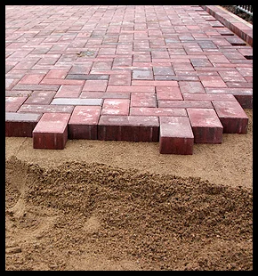 Red bricks being laid on sand to create a paved surface.