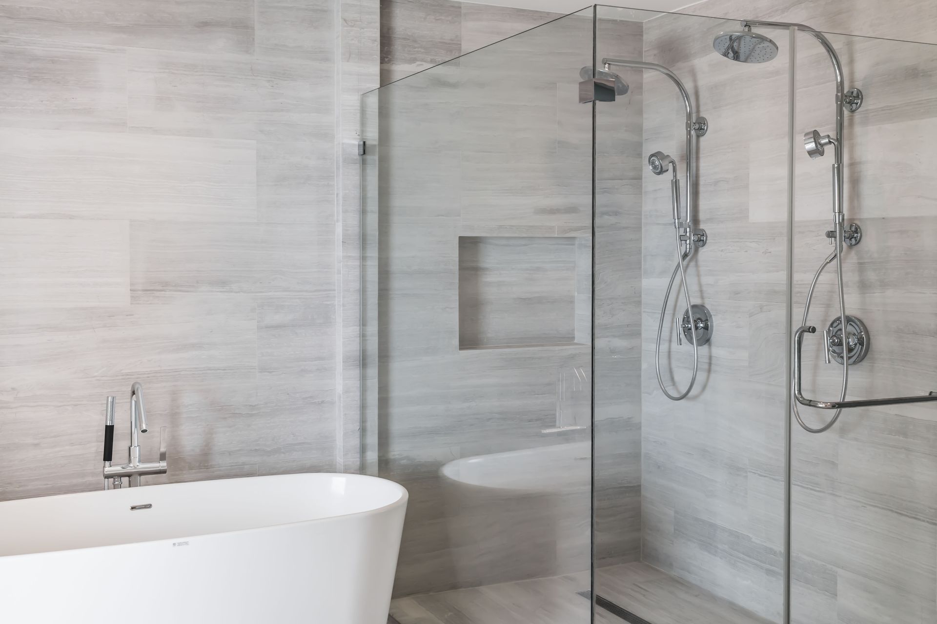 Modern bathroom with white tub, glass shower, and gray tile walls.