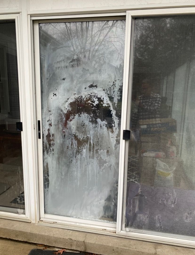 White-framed sliding glass door with frosted, smeared film obscuring view. Concrete base, outdoor setting.