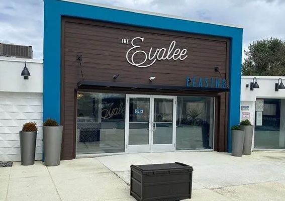 The Evalee restaurant exterior with a wood-paneled facade, blue trim, large glass doors, and two tall planters.