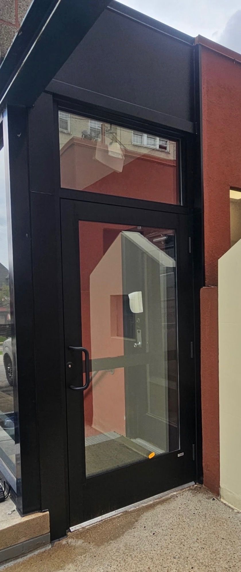 Modern glass-front entrance with black frame and red side panel under a dark awning