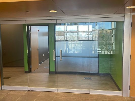 Glass entrance with sliding doors, inside a room with green walls and tile floor.