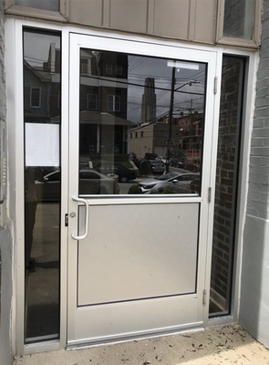 A silver commercial entrance door with glass panes and side panels, set into a brick building.