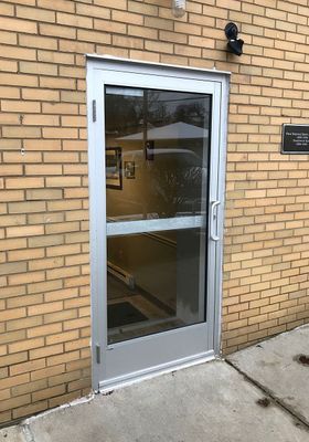 Exterior doorway with glass panel, silver frame, brick wall.