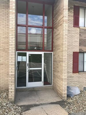 Brick building entrance with glass door and sidelights. Red-framed windows above. Red shutters on upper windows.