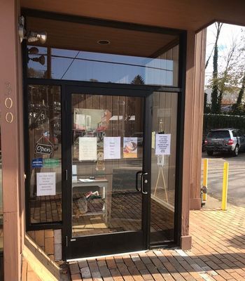 Exterior of a storefront with glass doors, signs, and a partially visible interior, with a car parked outside.