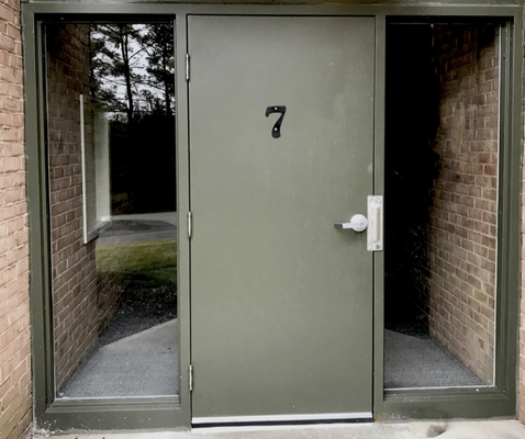 Apartment entry door with number 7, flanked by glass panels and brick walls.