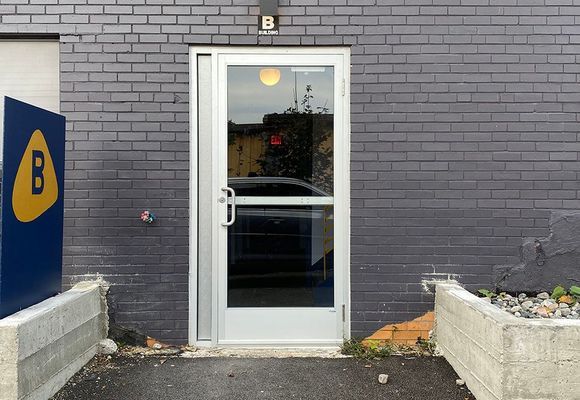 White door in gray brick building, with a blue sign featuring a yellow 