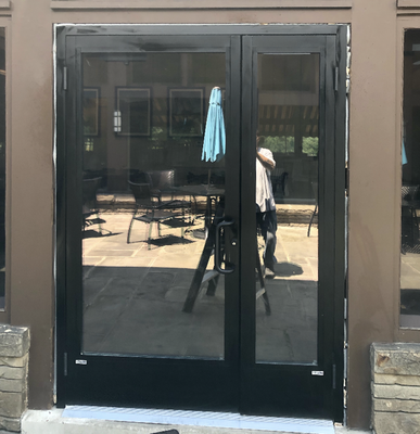Black glass double doors, reflecting outdoor seating area.