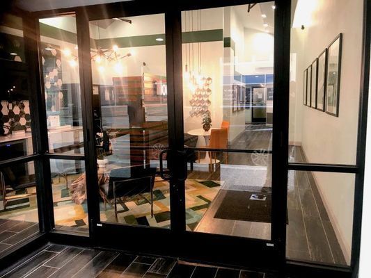 Glass doors leading into a modern office, showing interior decor and hallway with framed artwork.