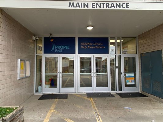 Main entrance of Propel East school. Silver doors, under a gray awning, with text and a logo.