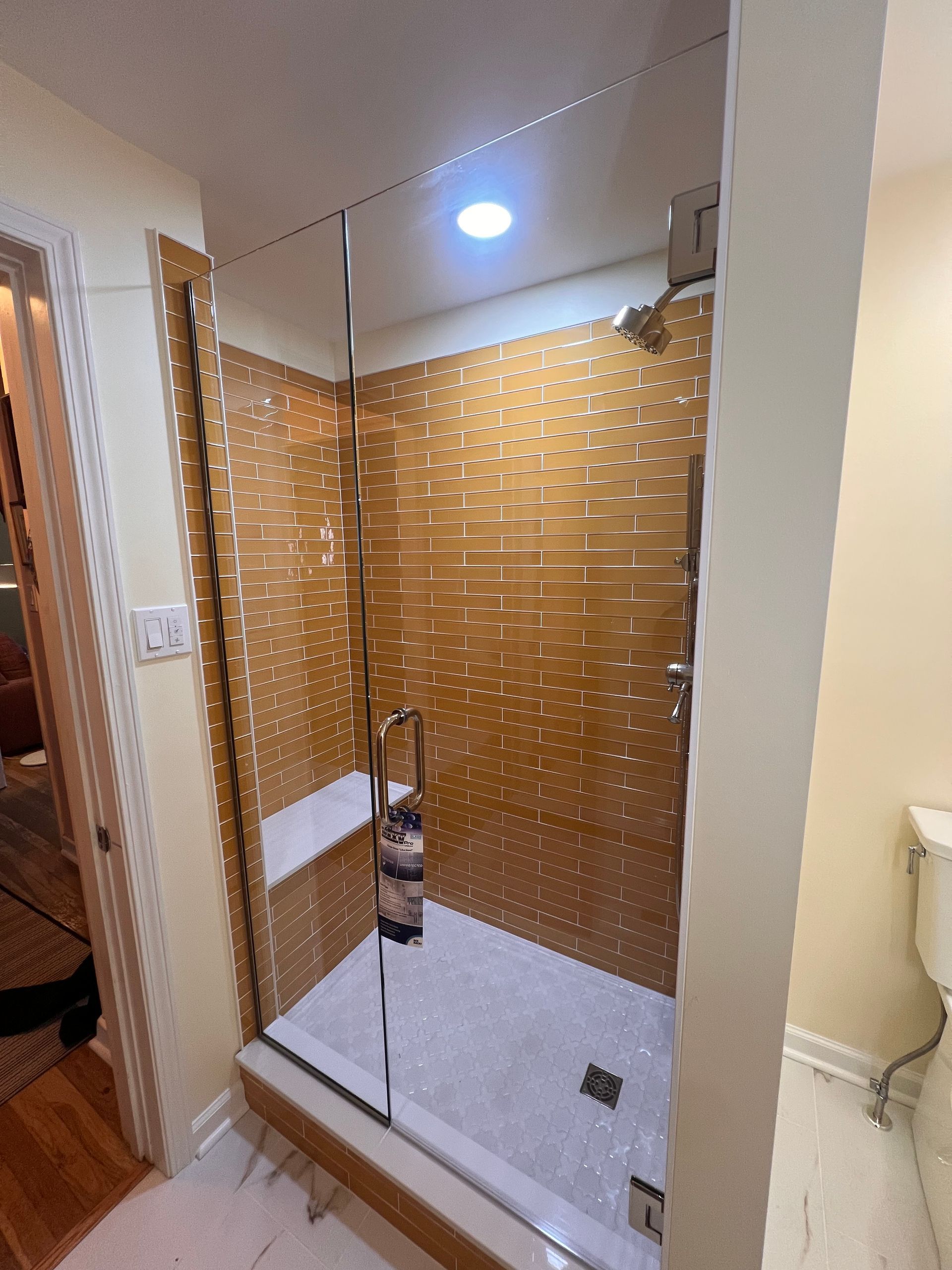 A walk-in shower with a glass door, light-colored tiled floor, and walls covered in textured, horizontal golden-brown tiles.