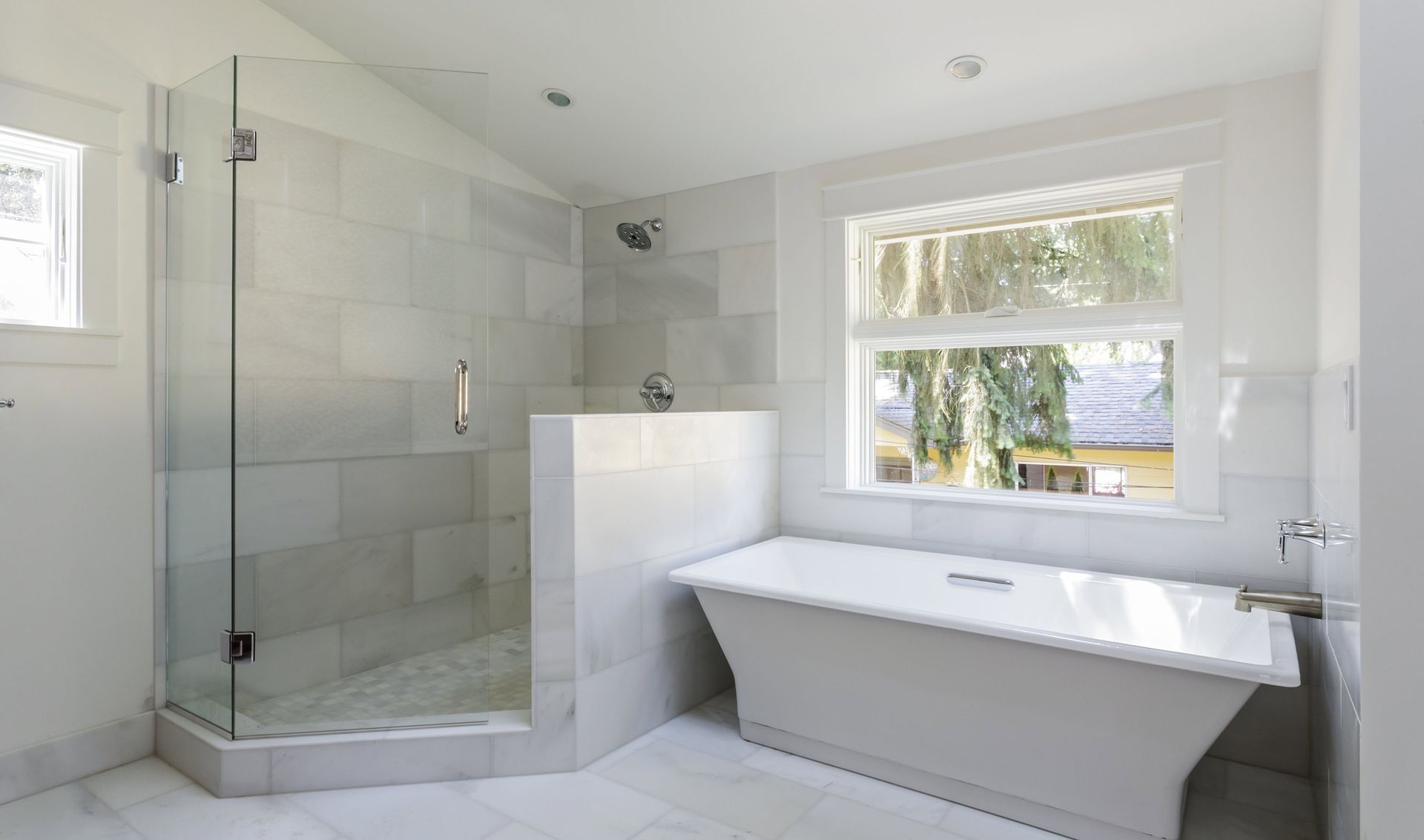 Modern white bathroom featuring a walk-in glass shower next to a freestanding soaking tub under a window.
