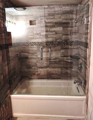 Shower with glass doors. White tub, gray and brown stone tile walls. Chrome fixtures.