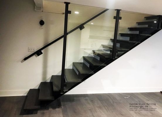 Black staircase with glass panel railing in a modern, white-walled interior.