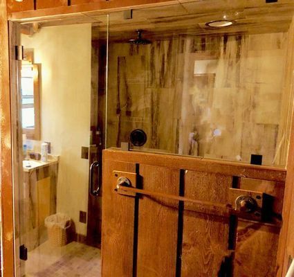 Wooden-framed glass shower enclosure with sliding wooden door, light brown wall and ceiling, tiled interior, showerhead visible.