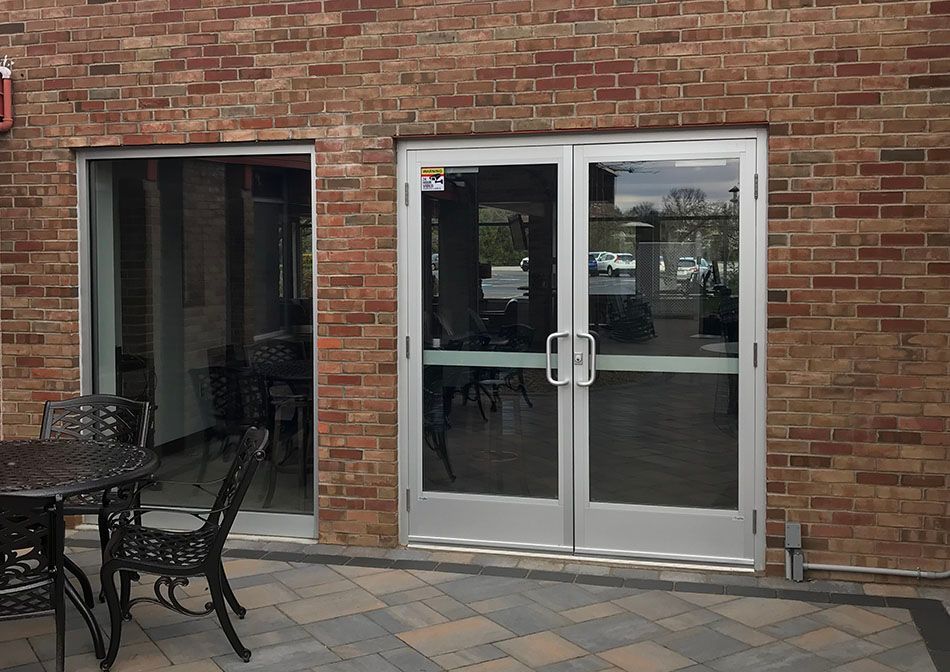 Exterior view of a building with brick walls. Glass doors lead inside. Patio furniture sits in front.