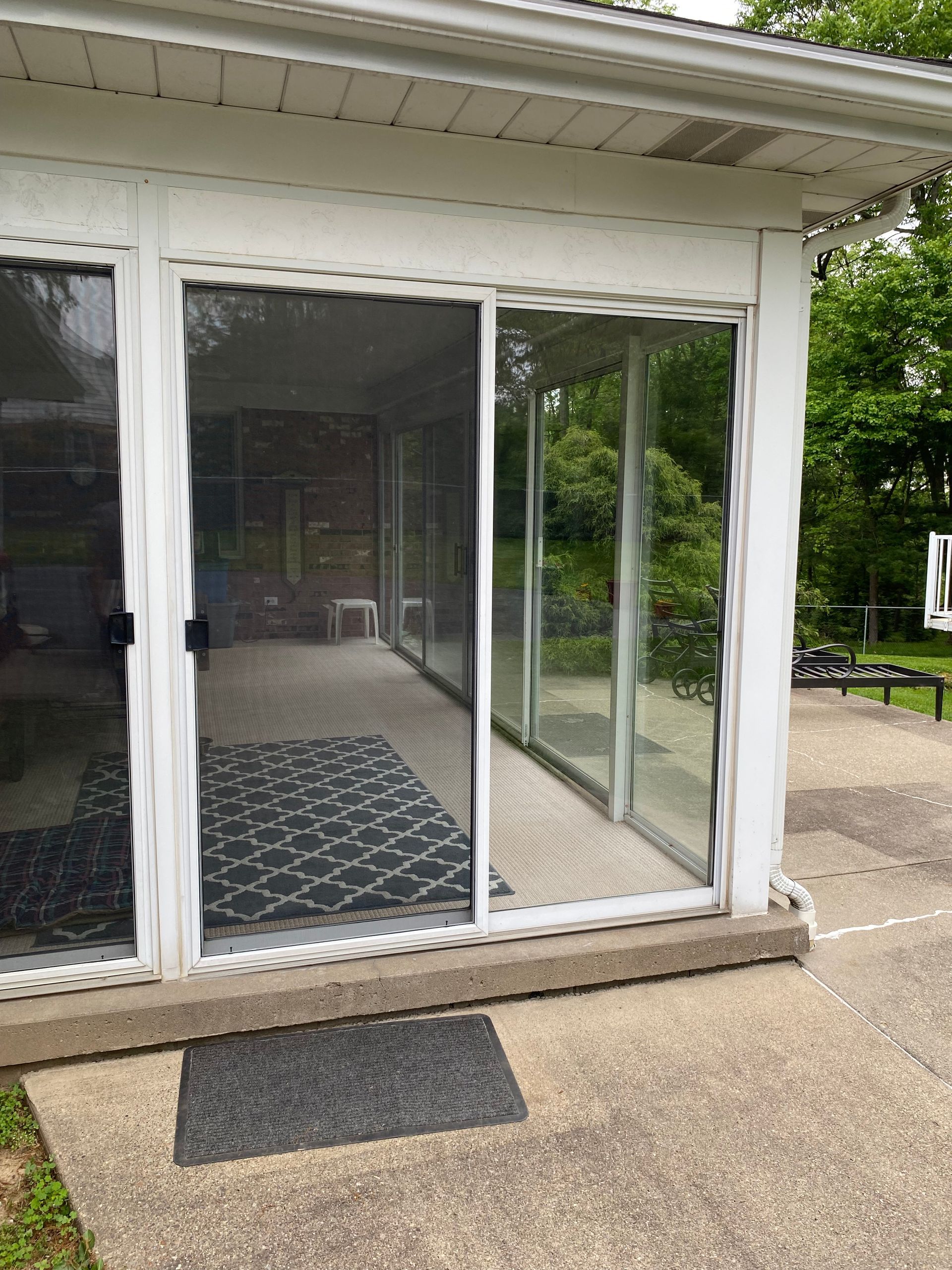 A white-framed screened porch with sliding glass doors, a patterned outdoor rug, and a concrete patio entrance.